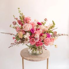 a vase filled with pink and white flowers on top of a wooden table next to a wall