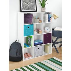 a white bookcase filled with lots of different colored boxes next to a green rug