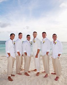 a group of men standing next to each other on top of a white sandy beach