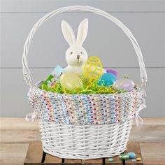 a basket filled with easter eggs and an bunny sitting in the center, on top of a wooden table