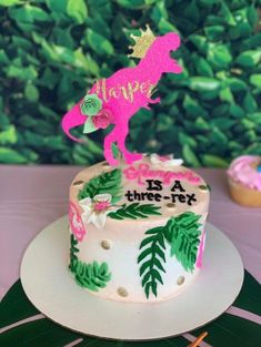 a birthday cake with a pink horse on top and green leaves around the edges that says happy is a three - fox