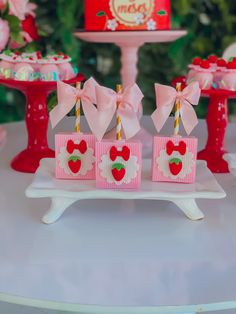 pink candy boxes with bows on them sitting on a white table in front of a cake