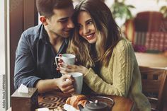 a man and woman sitting at a table holding coffee cups