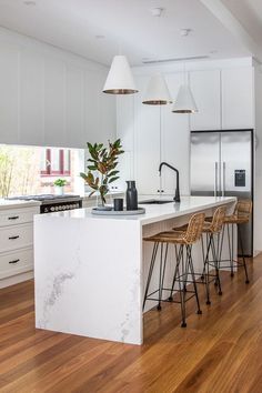 a kitchen with white cabinets and marble counter tops, two bar stools next to the island