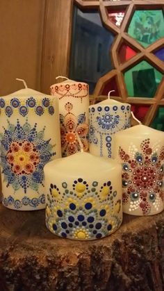 five candles with designs on them sitting on a tree stump in front of a stained glass window