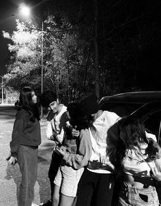 several people are standing around talking to each other in front of a car at night