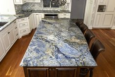 a large kitchen with white cabinets and blue marble counter tops, along with wooden floors