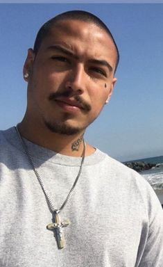 a man with a cross on his chest standing in front of the ocean and looking at the camera