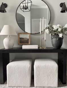 a black table with two white stools and a round mirror on the wall above it