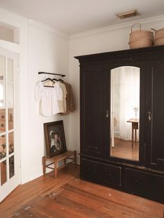 a large black armoire in the corner of a room with wooden floors and white walls