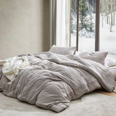 an unmade bed sitting on top of a wooden floor in front of a window