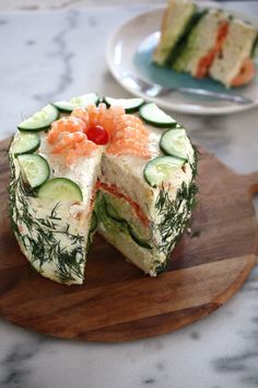 a cake with cucumber and salmon on it sitting on a wooden plate next to another piece of cake