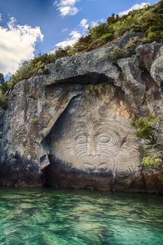 a rock face carved into the side of a cliff next to a body of water