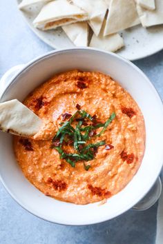 a white bowl filled with hummus and tortilla chips on top of a blue table