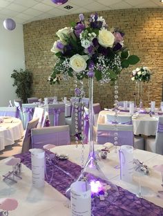 purple and white flowers are in a tall vase on the center table at a wedding reception