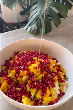 a white bowl filled with fruit on top of a table next to a potted plant