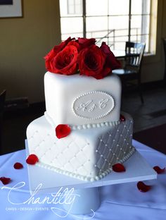 a three tiered cake with red roses on the top and initials on the bottom