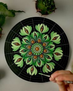 a person is holding a paintbrush in front of a painting on a black plate