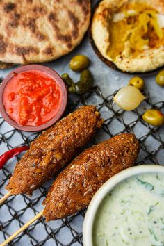 an assortment of food on a grill with sauces and pita bread in the background