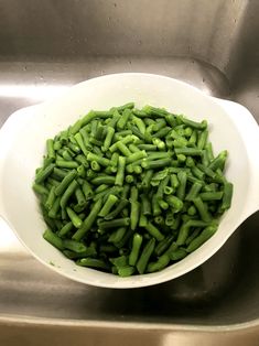 a bowl filled with green beans sitting on top of a metal sink