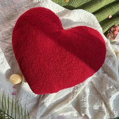 a red heart shaped pillow sitting on top of a white cloth next to a candle