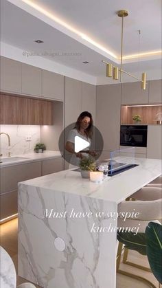 a woman is standing at the kitchen counter in front of an island with marble and gold accents