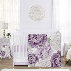 a baby crib bedding set with purple flowers on it and a mirror above the crib