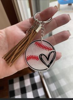 a hand holding a baseball keychain with a heart on it and a tassel