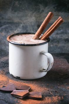 two cinnamon sticks sticking out of the top of a white cup filled with hot chocolate