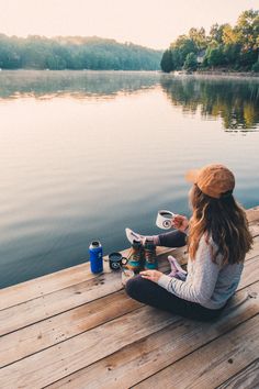 a woman sitting on a dock next to a lake