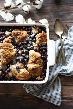 a blueberry cobbler in a white dish with cotton on the side and a spoon next to it