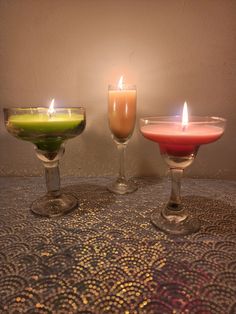 three different colored candles in glasses on a table