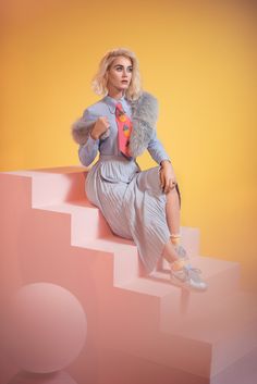 a woman sitting on top of a set of stairs wearing a skirt and jacket with feathers