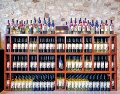 several shelves filled with different types of wine bottles on top of each other in front of a stone wall