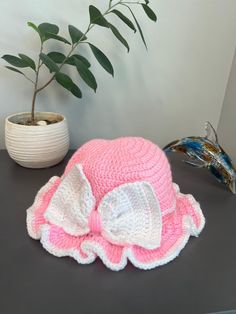 a crocheted pink and white hat next to a potted plant on a table