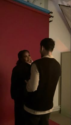 two people standing in front of a red wall