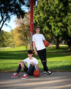 two young men sitting on the ground with basketballs