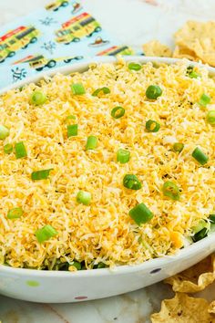 a white bowl filled with rice and green onions next to tortilla chips on a table