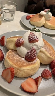 pancakes with whipped cream and strawberries are on a plate at a restaurant table, ready to be eaten