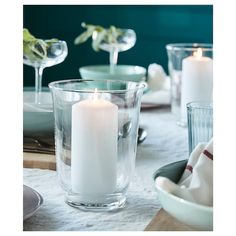 a white candle sitting in a glass vase on top of a table next to plates and glasses