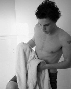 a shirtless man sitting on top of a towel in a bathroom