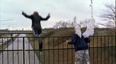 two people standing on the side of a road near a fence