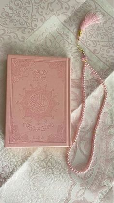 a pink book sitting on top of a bed next to a tasselled necklace