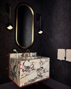 a bathroom with black walls and marble counter top, gold framed mirror above the sink