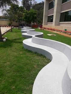 several curved concrete benches sitting on top of a grass covered field in front of a building