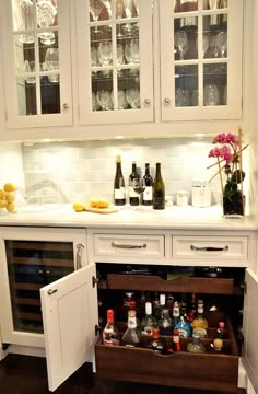 an open cabinet in the corner of a kitchen with wine glasses and bottles on it