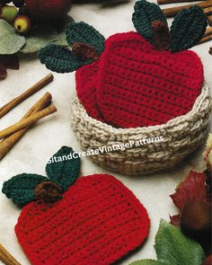 two knitted apples sitting in a basket next to cinnamon sticks and an apple with leaves