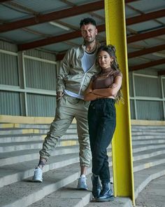 a man and woman standing next to each other in front of some bleachers