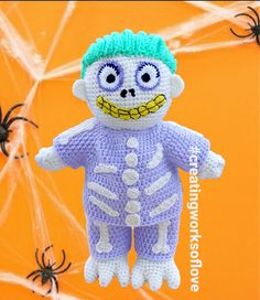 a crocheted skeleton doll hanging from a spider web on an orange background with black widowes