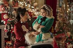 two women standing in front of a christmas tree holding a small dog and talking to each other